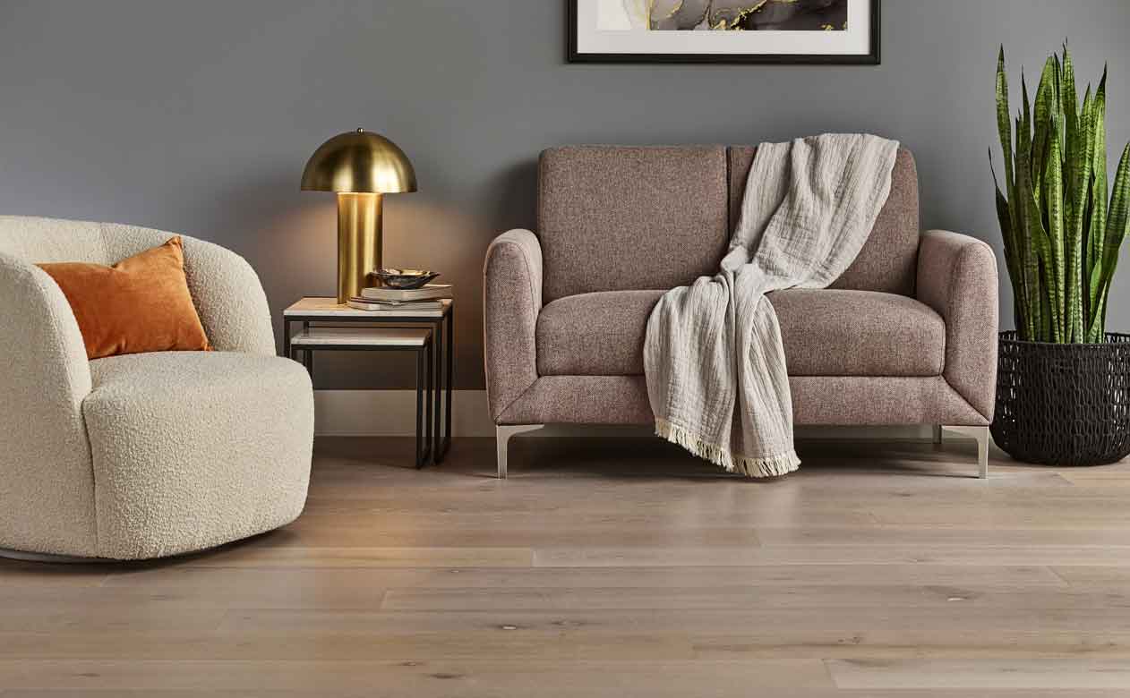 light multi-toned hardwood wide plank flooring in sitting area with white swivel chair and brown sofa